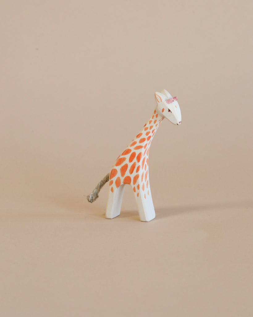 A small Ostheimer Small Giraffe - Head Low stands on a plain light beige background, painted with detailed orange spots and a slight pink detail on the ears.