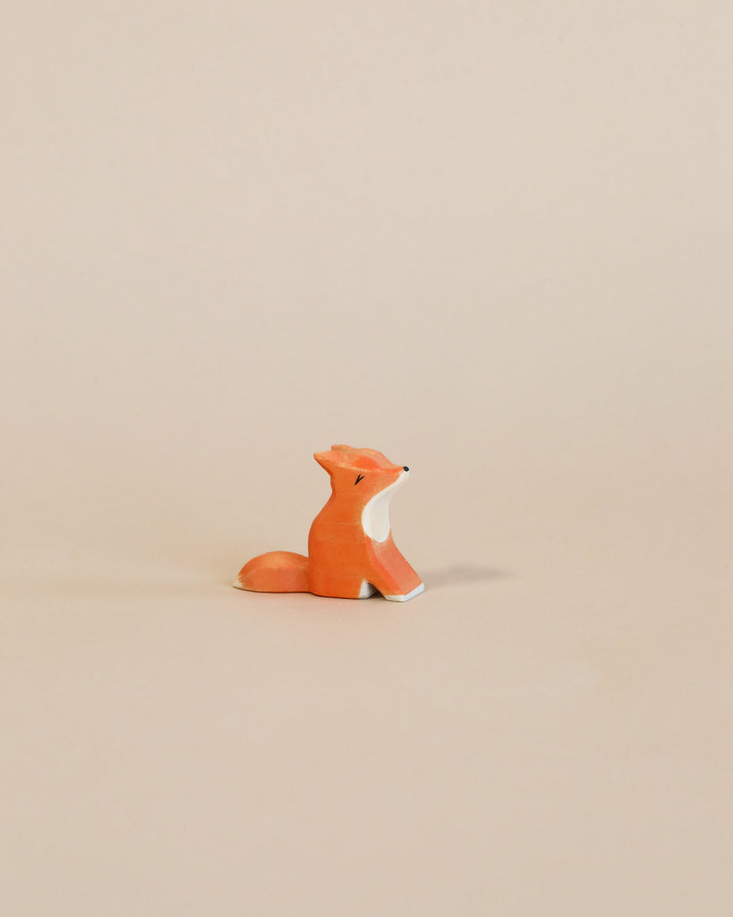 A small, handcrafted Ostheimer wooden figurine of a fox sitting on a plain beige background, looking upwards with a thoughtful expression.