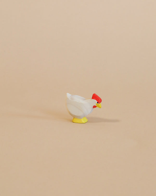 A small, handcrafted Ostheimer White Hen - Standing with a white body, red head, and yellow feet stands isolated against a plain beige background.