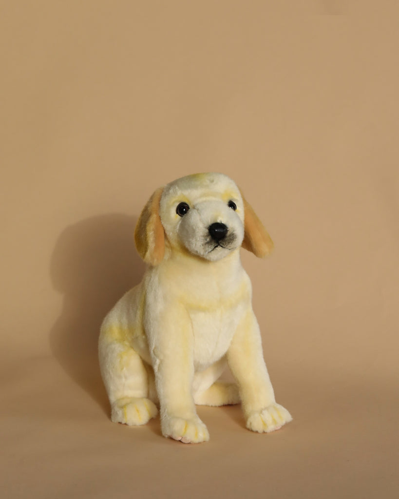 A Labrador Dog Stuffed Animal sits on a plain beige background. The realistic plush animal has soft, light yellow fur, floppy ears, and a lifelike expression resembling a puppy. Its hand-sewn details and unique features make it look exceptionally cute.