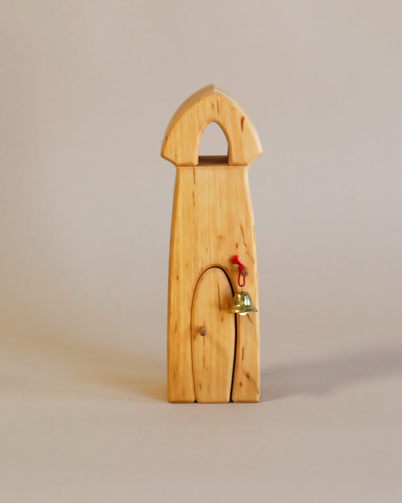 A handcrafted Ostheimer Sentry Post With Bell, featuring an arched top and a small, hanging brass bell next to a red door handle, set against a plain, light background.