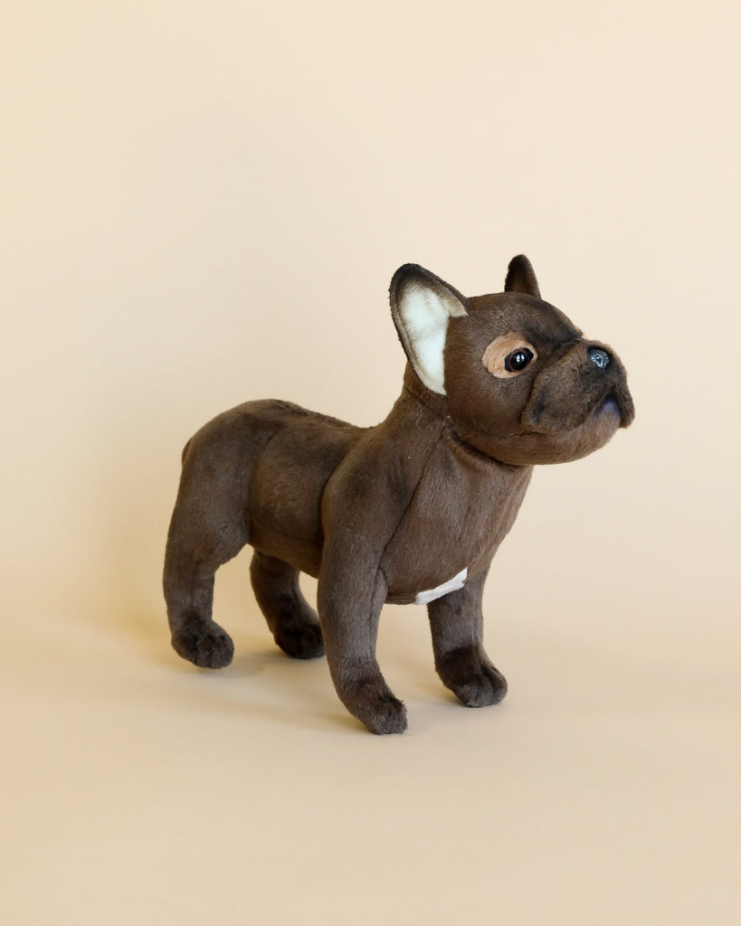 A French Bulldog Dog Stuffed Animal, standing profile with a brown coat and attentive expression, crafted from high quality materials set against a plain light beige background.