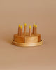 The Handmade Wooden Cake, crafted from pear wood in Ukraine, includes eight yellow candles and is set against a beige background. The cake is divided into four pieces, each holding two candles. It has a simple and natural design with a smooth finish, making it an enchanting children's candle holder ideal for imaginative play.