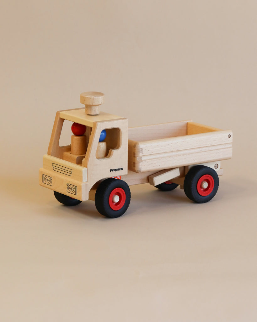 A Fagus wooden dump truck with a beige cab and an open back cargo area, featuring red wheels, and blue and red wooden beads in the driver's seat, on a neutral background.