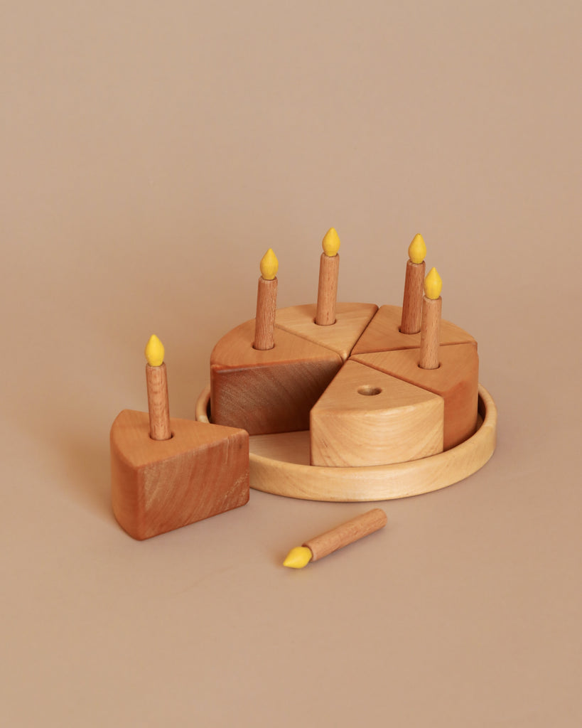 A Handmade Wooden Cake set featuring six slices, meticulously crafted from pear wood in Ukraine. Five of the slices include small, detachable candle holders with yellow flames. One slice sits outside the circular wooden base, and a separate candle lies beside the cake.