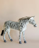 The Large Zebra Stuffed Animal, featuring realistic black and white stripes, stands out beautifully against a neutral beige background. Lovingly hand-sewn, it includes a fluffy mane and grey hooves, giving this zebra its own unique personality.