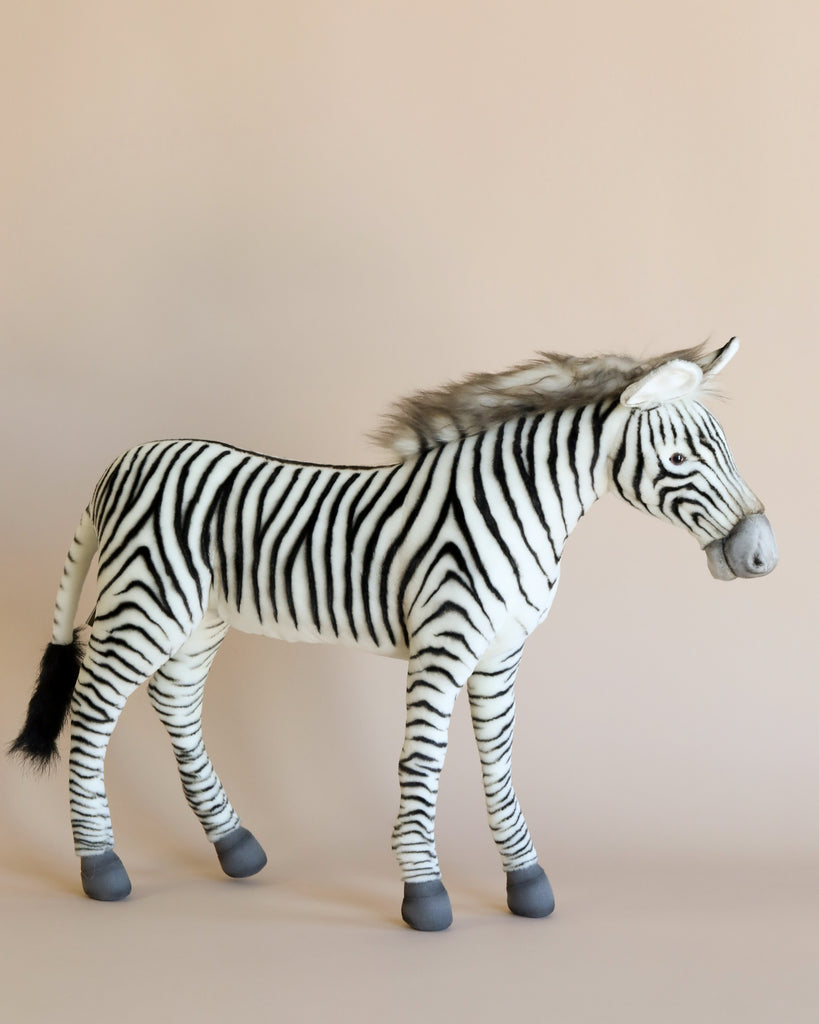 The Large Zebra Stuffed Animal, featuring realistic black and white stripes, stands out beautifully against a neutral beige background. Lovingly hand-sewn, it includes a fluffy mane and grey hooves, giving this zebra its own unique personality.