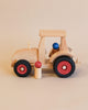 A Fagus Wooden Modern Tractor with red wheels and a light beige body, featuring a blue ball as a driver and a red mushroom-shaped figure beside it.