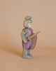 The Ostheimer Red Knight - Standing, a wooden toy figure handcrafted from sustainably sourced materials, is depicted in profile view, facing left. The knight is adorned in a silver and purple outfit, holding a sword in one hand and a purple shield in the other. The background is a plain light beige color.