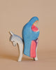 The Ostheimer Mary on Donkey is a small wooden figurine depicting a person in a blue and red cloak riding a white donkey. The art style is minimalist, with bold colors and smooth lines. Perfect for imaginative play, this piece reflects the timeless charm of handcrafted toys against a plain, light beige background.