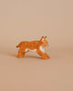 The Ostheimer Lynx Running is a small, handcrafted wooden figurine featuring an orange lynx adorned with black spots and white highlights. Made from sustainably sourced materials, the lynx is depicted in a stretched, low stance with its ears pointed upward and eyes closed, set against a soft beige background.