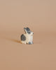 Against a beige background sits the Ostheimer Black & White Rabbit - Sitting, a small, carved wooden figurine reminiscent of quality craftsmanship. Painted in elegant shades of white and gray, this rabbit boasts a simple, minimalist design that encourages imaginative play with handcrafted wooden toys.