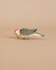 The Ostheimer Woodpecker, a small wooden bird figurine with a red head and gray wings, stands gracefully on a beige surface. Crafted in a minimalistic style with smooth lines and muted colors, this piece exemplifies the exquisite use of sustainably sourced materials often found in handcrafted wooden toys.