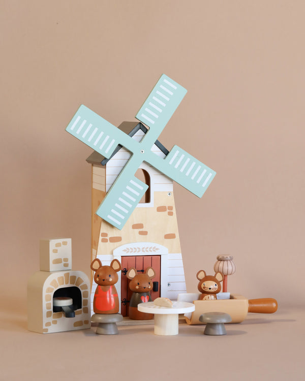 A Penny Windmill set against a beige background, accompanied by small wooden animal figures, a fireplace, and cooking utensils. The scene evokes a rustic, playful ambiance suitable for imaginative play.