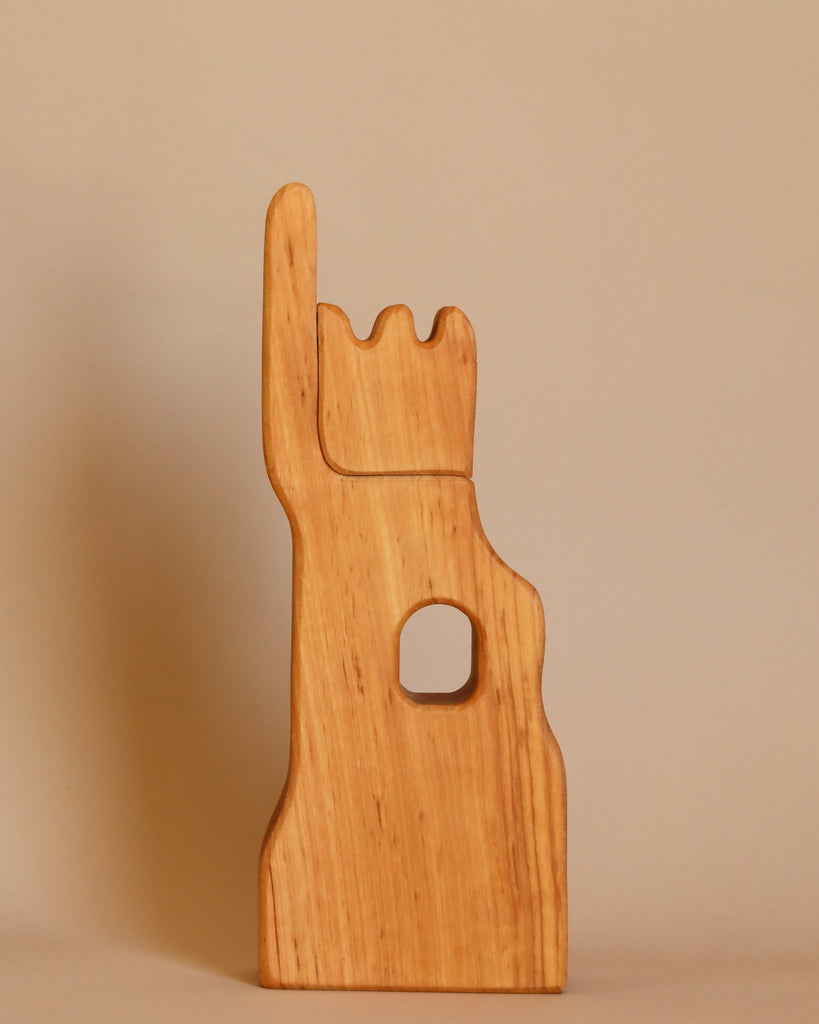 The Ostheimer Lookout - Small is a wooden sculpture shaped like a hand with the index finger raised and the other fingers folded down. This imaginative play piece also features a circular hole in the palm area and is set against a plain beige background.