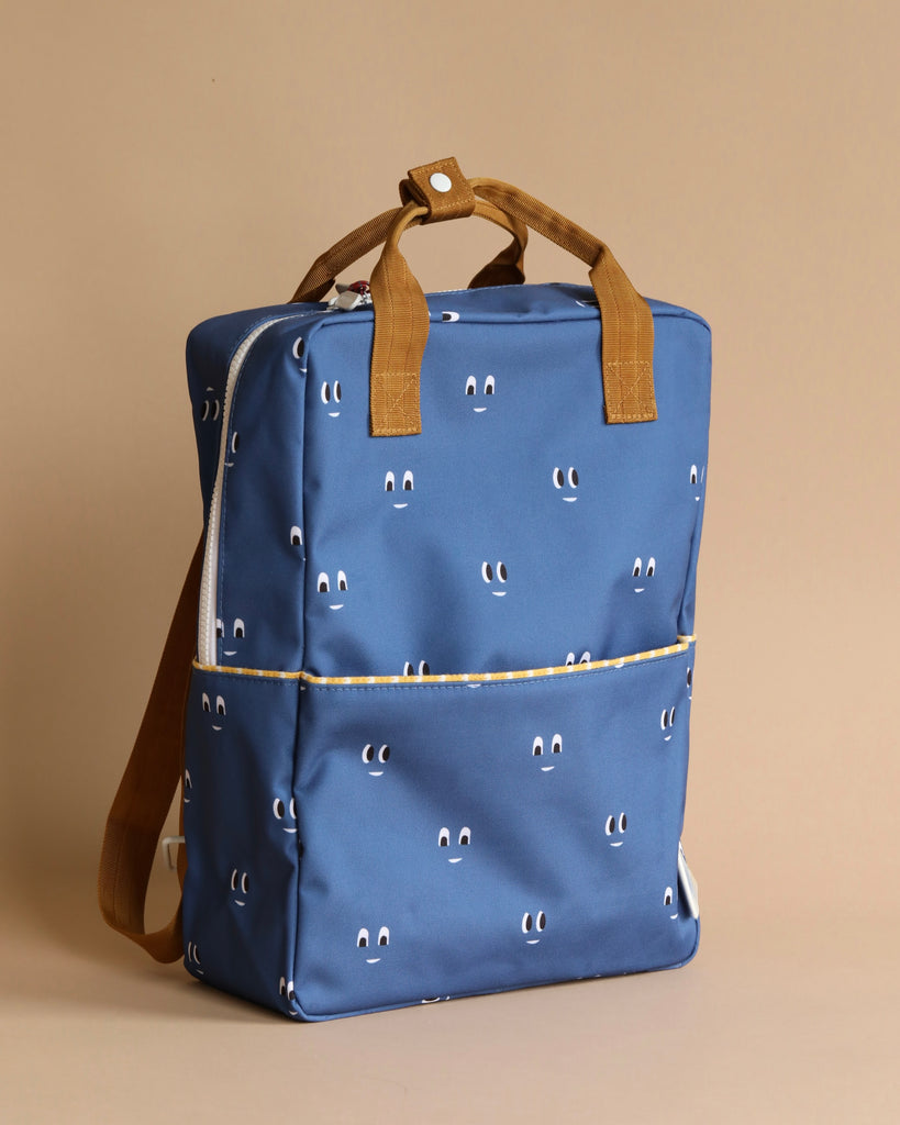 The Sticky Lemon Backpack Large, Special Edition Eyes in Boxing Blue, is crafted from recycled PET bottles and features a playful pattern of small, white smiling faces. It includes tan handles, a front pocket, and waterproof lining. Positioned against a beige background, this stylish and eco-friendly backpack is both fashionable and sustainable.