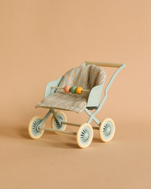 A small vintage-style Maileg Stroller, Baby Mice - Blue on a beige background, perfect for mouse families. The stroller has a light blue frame, off-white wheels, and a fabric seat with a striped pattern. It features a wooden bead bar across the front, ideal to transport babies in charming style.