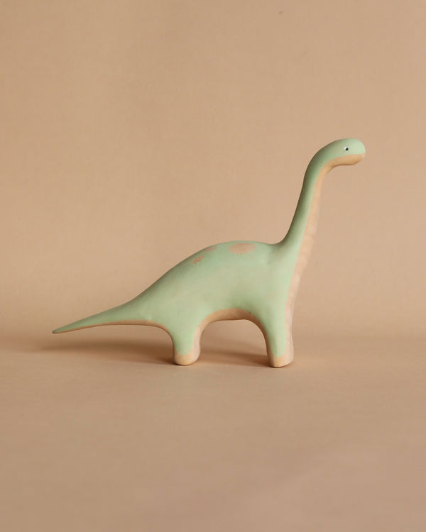 A small, handmade wooden Brachiosaurus dinosaur figurine with a long neck and tail, standing against a plain beige background.