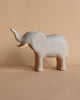 A small, simple Handmade Wooden Elephant stands on a neutral beige background. The elephant, with its trunk raised, has a minimalist design with smooth surfaces and light detailing, resembling handcrafted toys, giving it a serene appearance.