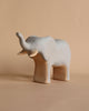 A Handmade Wooden Elephant with its trunk raised stands against a plain beige background. Carefully crafted with child-safe paint, the minimalist design showcases its smooth surface and simple features.