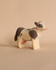 A Handmade Wooden Cow, handcrafted from linden wood, stands on a tan surface. Painted with black and white patches using child-safe paint, the figurine features a charming design with a pink udder and a minimalistic facial expression. Handmade in Serbia, the background is a solid beige color.