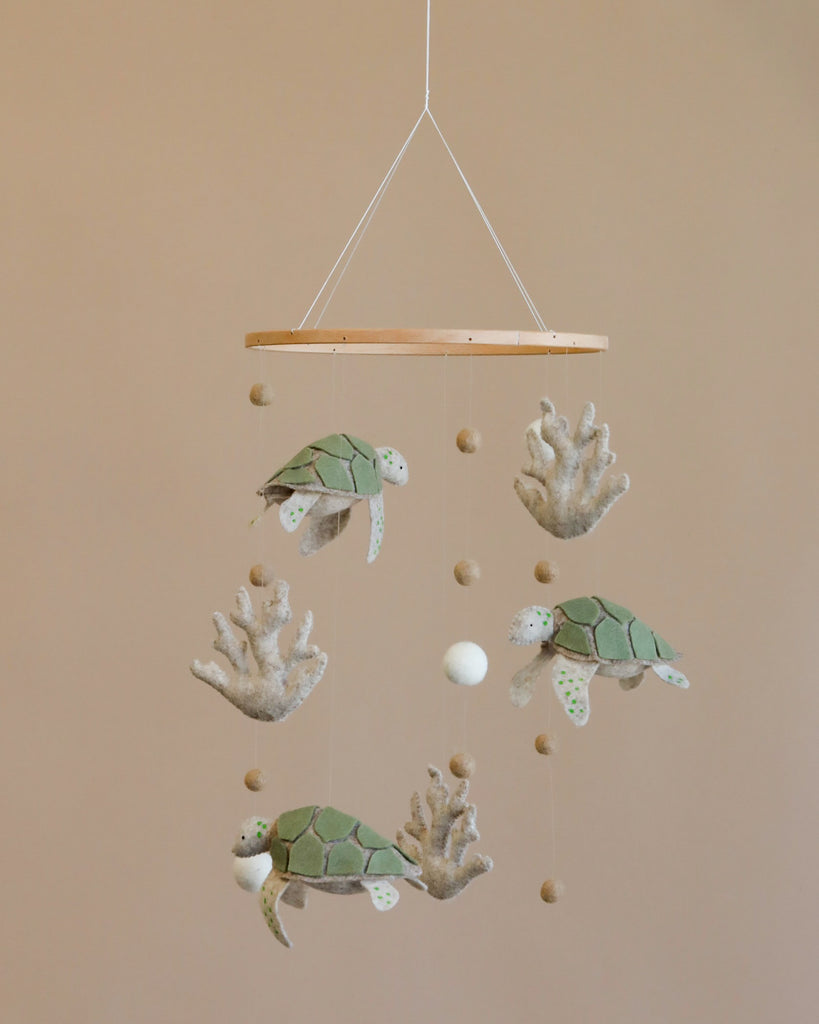 A Handmade Mobile - Ocean Turtles - Final Sale featuring four plush sea turtles and several small felt balls suspended from a wooden ring against a light beige background.