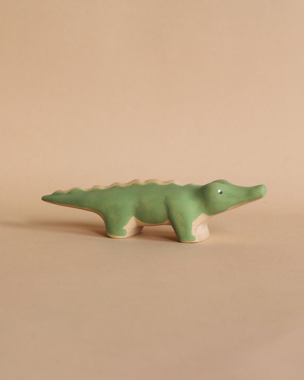 A small, green Handmade Wooden Crocodile with a streamlined body and minimalistic features, including small eyes and subtly carved legs, stands against a plain beige background. Handcrafted with non-toxic paint, this charming crocodile's simple and smooth design makes it an ideal child-safe toy.