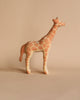 A small, light-brown Handmade Wooden Giraffe with darker brown spots stands on a beige background. Handmade in Serbia from linden wood and adorned with child-safe paint, the giraffe has a simple, smooth design with minimal details, giving it a cute and whimsical appearance.