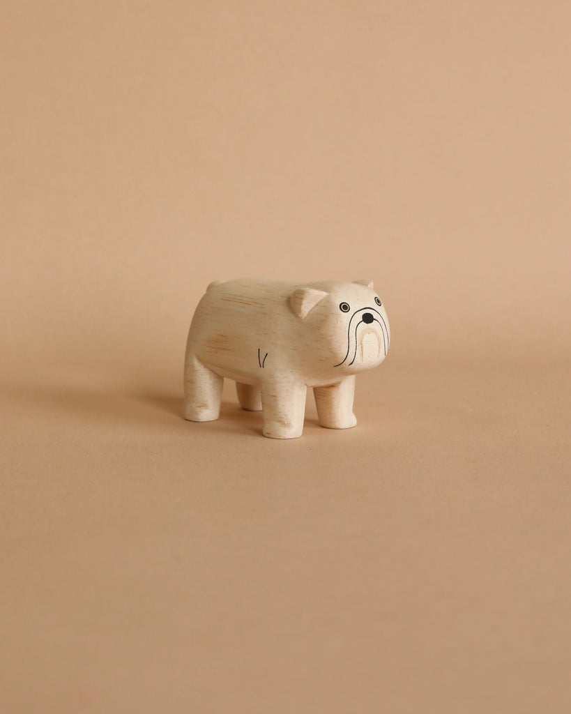 A small, hand-carved wooden bulldog figurine with visible wood grain, featuring large cartoon-style eyes and a curved trunk, stands against a plain beige background.