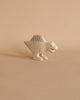 A small, light-colored Handmade Tiny Wooden Spinosaurus Dinosaur stands on a neutral, pale background. The dinosaur has a simple, minimalist design with a rounded body, four legs, a large tail, and minimal facial features. This unique handcrafted decoration pairs beautifully with hand-carved wooden animals for an eco-friendly touch.