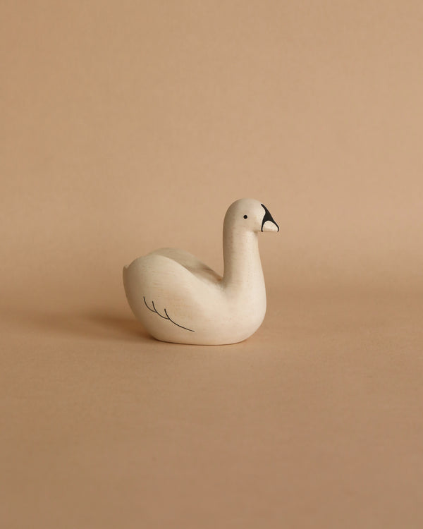 A small, minimalist white Handmade Tiny Wooden Swan with a black beak and simple black line details on the wings, hand-carved from Falcata wood. The background is a plain, light beige color.