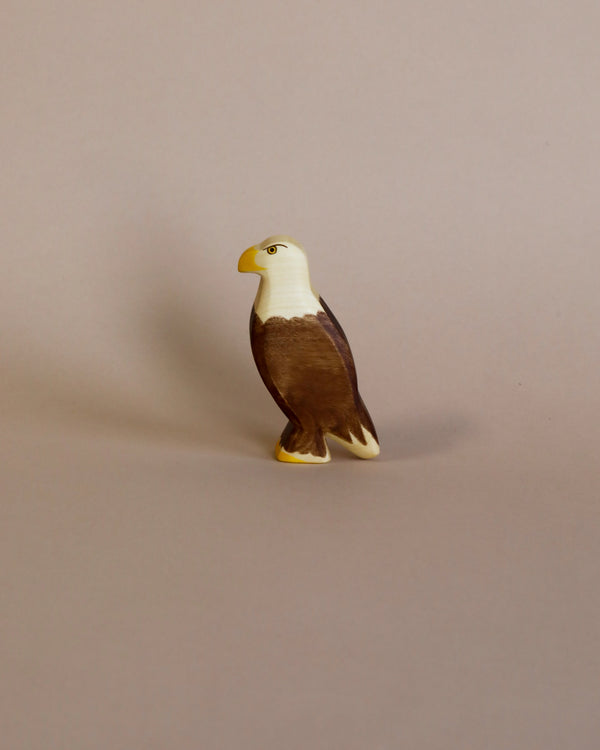 A small, detailed Handmade Holzwald Eagle standing upright on a plain beige background, crafted from sustainable wooden materials.