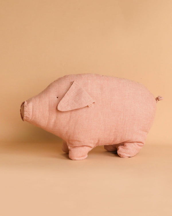 A Maileg classic, the Maileg Polly Pork, Medium made of pink checkered material stands on a neutral beige background. With small round ears, a stitched snout, and a curly tail, it exudes a cuddly charm. The plush pig is filled with recycled polyester for an eco-friendly touch.