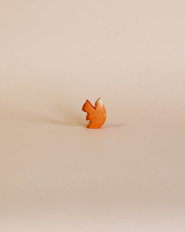 A small, uniquely shaped Handmade Holzwald Small Squirrel stands upright against a plain, light beige background, suggesting it could inspire sustainable toys.