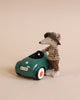 A Maileg Mouse Car - Dark Green, dressed in a knitted sweater and a hat, sitting in against a beige background.