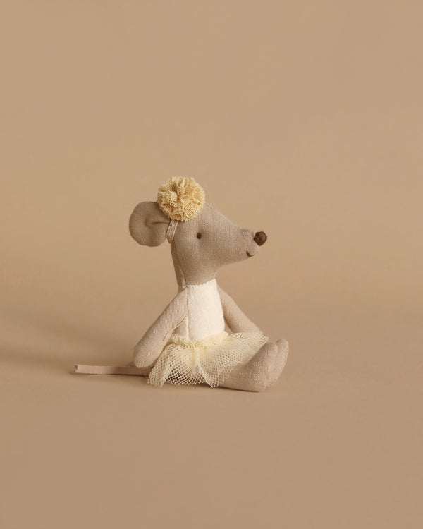 The Maileg Ballerina Mouse - Little Sister (Off White) is a stuffed ballerina mouse toy dressed in a white tutu and adorned with a yellow flower on its head. Positioned slightly to the side against a beige background, it provides a charming profile view. Made from soft cotton, this delightful little sister mouse is perfect for any collection.