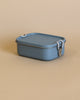 A Haps Nordic - Stainless Steel Lunch Box - Ocean with a matching lid secured by white clasps sits on a light tan surface.