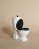 A Maileg Miniature Toilet - Teddy Size with a black seat and black lid in the raised position. It has a sleek, simple design, perfect for any bathroom assortment, set against a plain beige background.