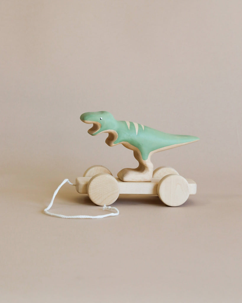 A Handmade Wooden T-Rex Dinosaur Push Toy With Built-In Magnets, with a green-painted body, handcrafted from linden wood, is placed on a neutral background. The dinosaur figure is mounted on a platform with four wheels and has a white string attached for pulling. Non-toxic paint ensures it's safe for kids to enjoy.