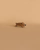 A small, light brown wooden figurine of a wild boar in a playful stance, handcrafted by Ostheimer, placed on a beige background.