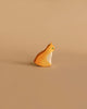 The Ostheimer Orange Cat, Sitting is a small, carved wooden figurine featuring an orange and white cat on a beige background. Reminiscent of traditional Ostheimer toys, this cat is depicted in a sitting position facing right. It has minimalistic features and a smooth finish, representing an excellent example of handcrafted wooden toys made from sustainably sourced materials.