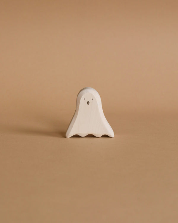 The Wooden Standing Ghost, a small and simple figurine made from sustainable hardwood, sits centered against a light brown background. This handmade ghost features two dot eyes and a wavy bottom edge, offering minimal details for a clean and charming appearance—perfect as a Halloween decoration.