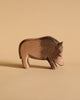 The Ostheimer Wild Boar, a carved wooden figurine, stands against a plain beige background. Handcrafted wooden toys like this one, featuring simple geometric shapes and detailed wood grain texture, are perfect for imaginative play. Crafted from sustainably sourced materials, it embodies both artistry and eco-consciousness.