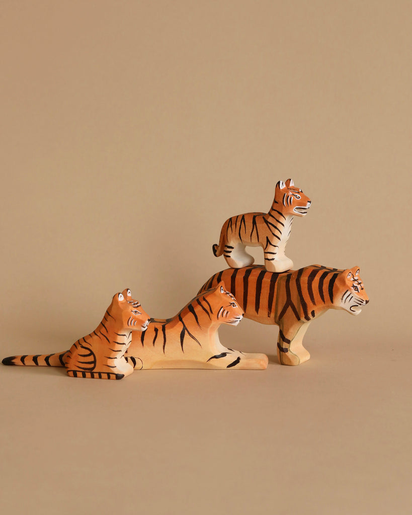 The Bumbu Wooden Tiger Set includes four beautifully handcrafted wooden tiger toys displayed against a simple beige background. One tiger is creatively balanced on top of another, which is reclining. Additionally, two tigers crafted from sustainable, eco-friendly materials are arranged side by side—one lying down and the other sitting upright.