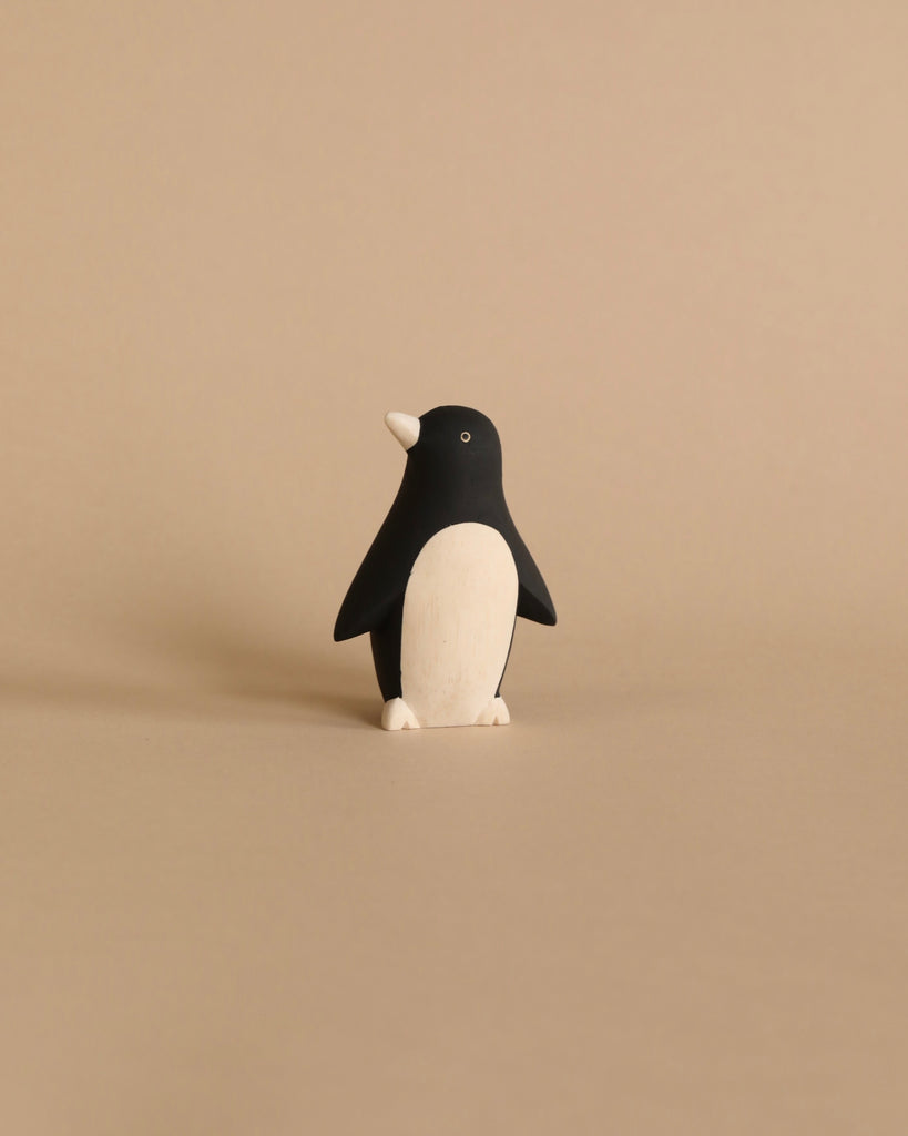 A small, minimalist Handmade Tiny Wooden Penguin stands upright against a light beige background. Handcrafted from Albizia wood, the penguin has a black head and back, white front, and small, simplistic features.