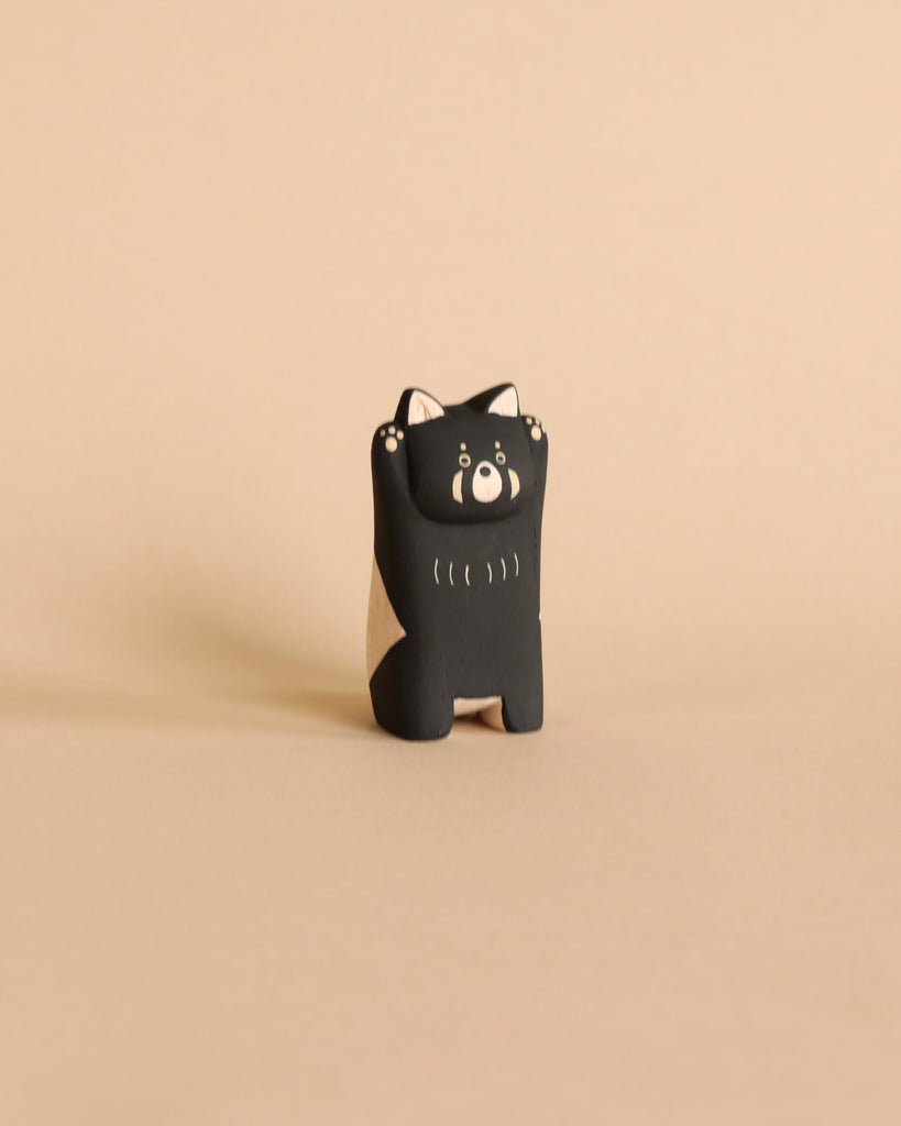 A small, wooden toy figurine resembling a red panda stands on a beige background. Handcrafted by Bali artisans, the red panda has a cute, smiling face with tiny eyes and raised arms, giving it a playful and inviting appearance. Made from Albizia wood, the overall setting is minimalistic and clean.