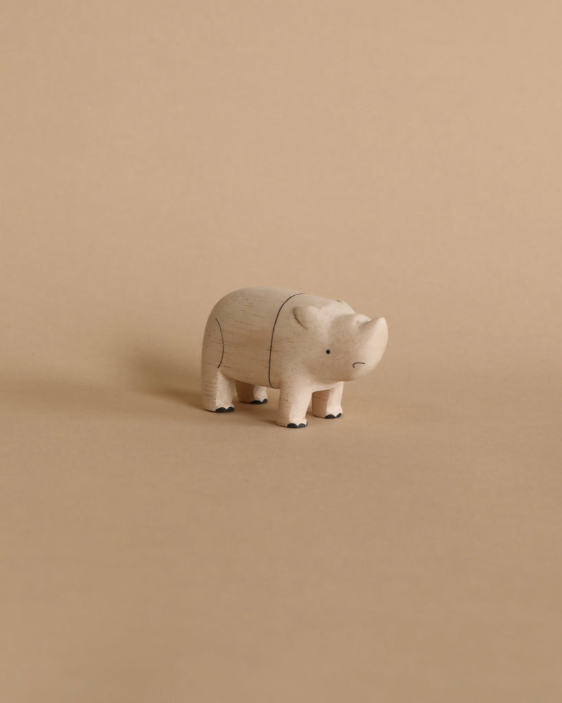 A small, light-colored Handmade Tiny Wooden Safari Animals - Rhino stands on a plain beige background. This handcrafted wooden rhinoceros, part of a curated collection of safari animals, features simple painted details like a small face and tiny feet. The image exudes a minimalistic and neutral tone.