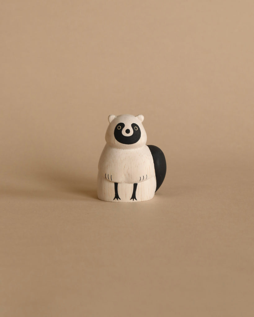 Placed against a plain beige background, the "Handmade Tiny Wooden Forest Animals - Raccoon" figure is crafted from Albizia wood in a simple, minimalist design. The white-bodied raccoon features black tail, eyes, and mask-like markings around its eyes, highlighting the meticulous craftsmanship of skilled artisans dedicated to creating these handcrafted wooden animals.