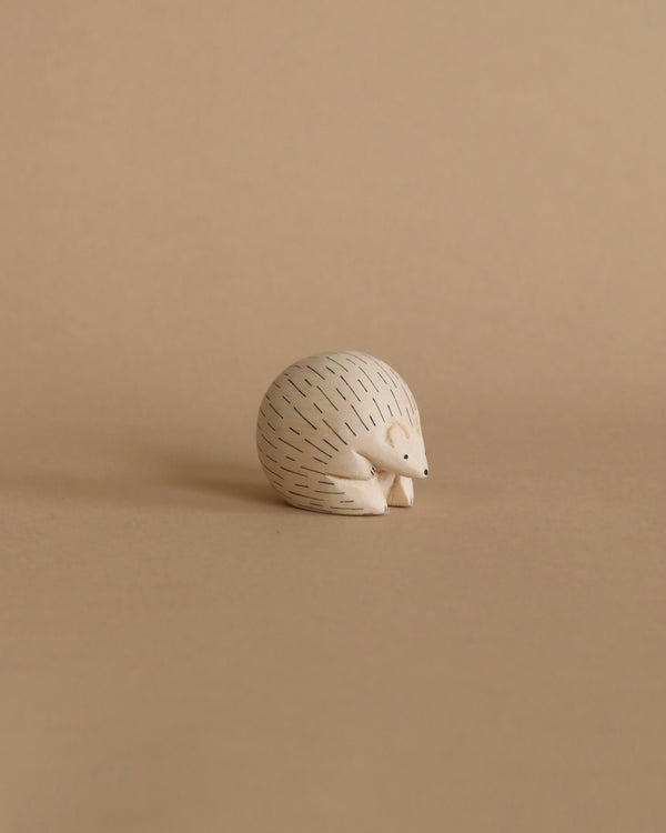 An intricately hand-painted, tiny wooden hedgehog figurine, featuring a minimalist design with a white body and black dotted lines to represent spines. This unique piece of art is part of the Handmade Tiny Wooden Forest Animals collection and is showcased against a simple, beige background.