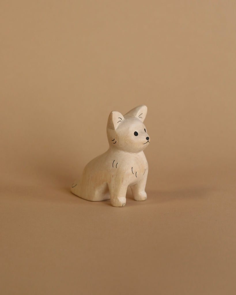 A small, handcrafted figurine of a Handmade Tiny Wooden Chihuahua with delicate facial features sitting against a plain beige background. The Chihuahua, carved from Albizia wood, has subtle black detailing for its eyes, whisk.